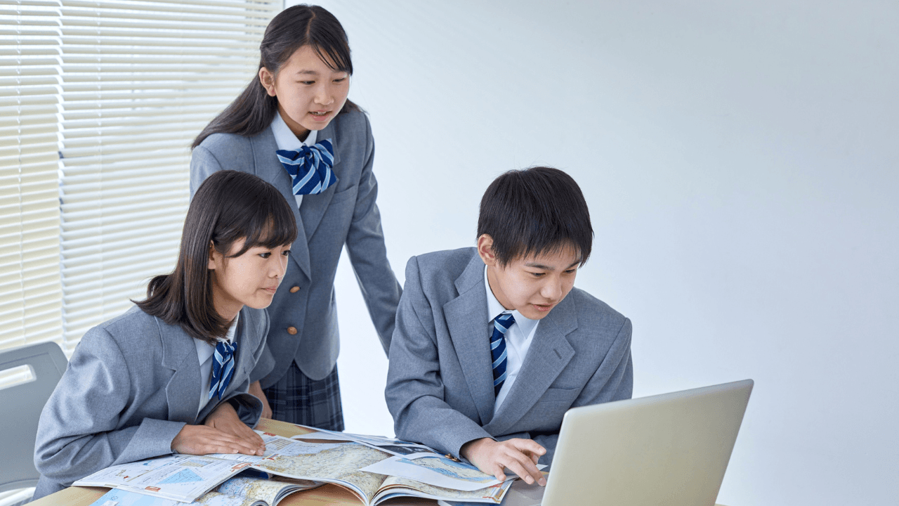 地図とノートPCを見ながら話し合う中学生
